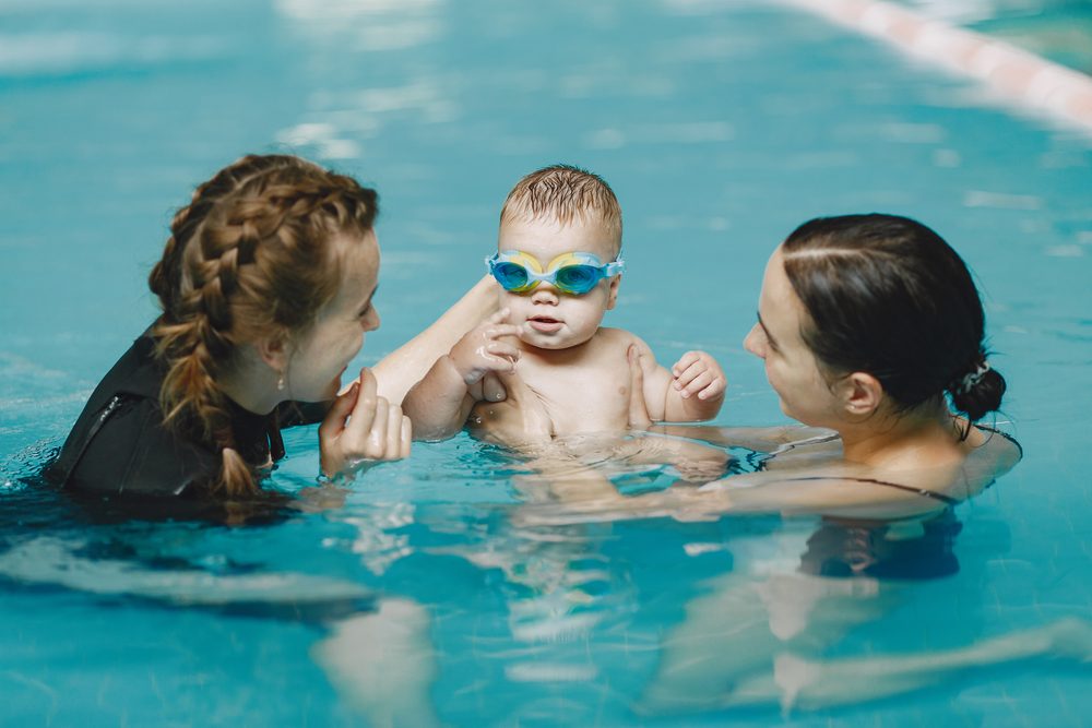 Baby im Schwimmbecken mit Mutter und einer Kursleiterin